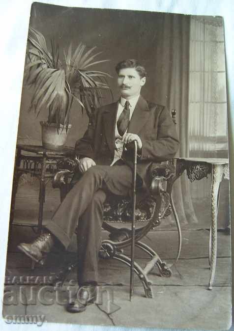 An old photo of a man with a cane is sitting
