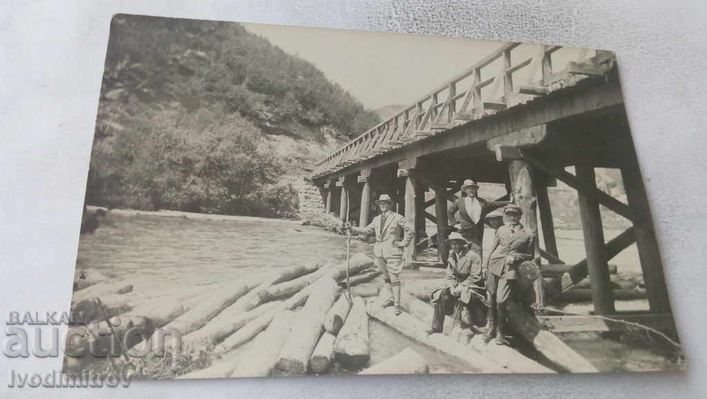 Photo Four men on logs by a wooden bridge
