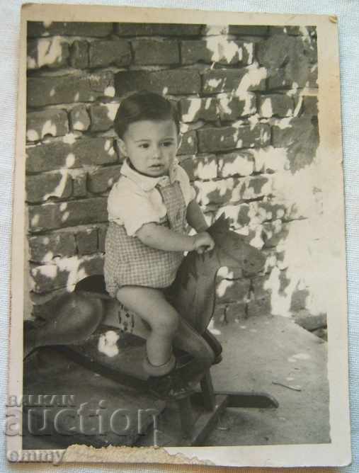 Μικρή παλιά φωτογραφία ενός παιδιού σε μια ξύλινη κούνια αλόγων