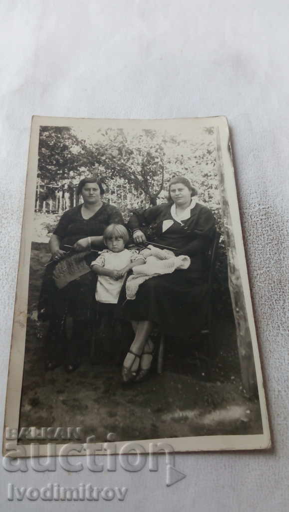 Photo Two women with knitting needles and a little girl in the garden