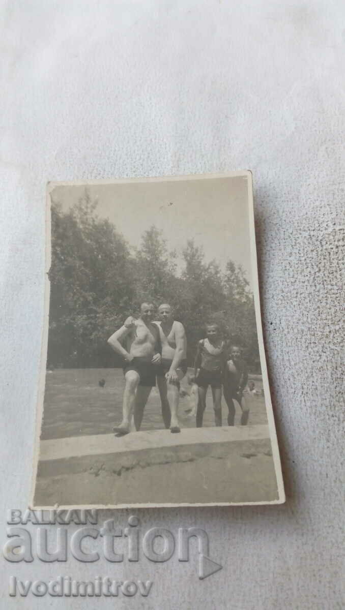 Photo Two men and two children in swimsuits at the pool