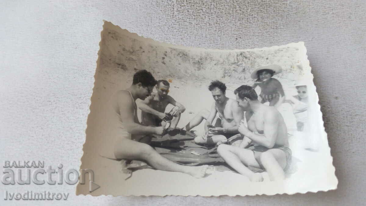 Photo Four men in swimsuits playing Bridge Belote on the beach