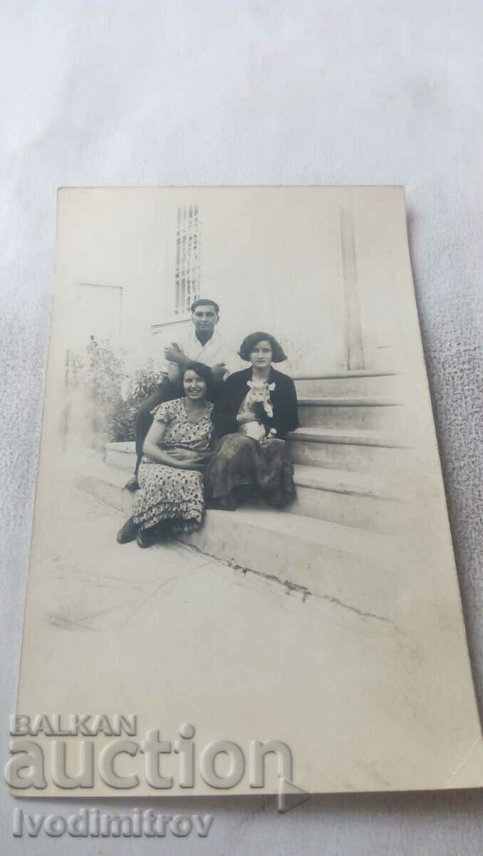 Fotografie cu un bărbat și două femei cu un pisoi mic pe scări