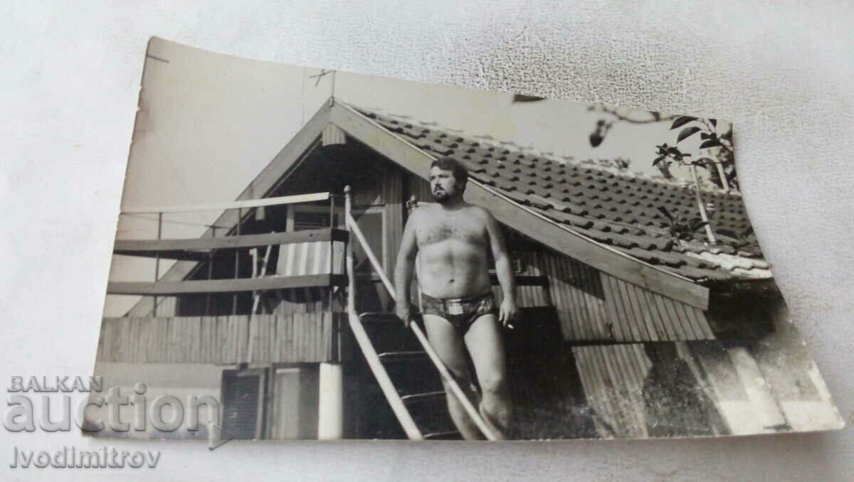 Fotografie cu un bărbat în costum de baie în fața unui bungalou