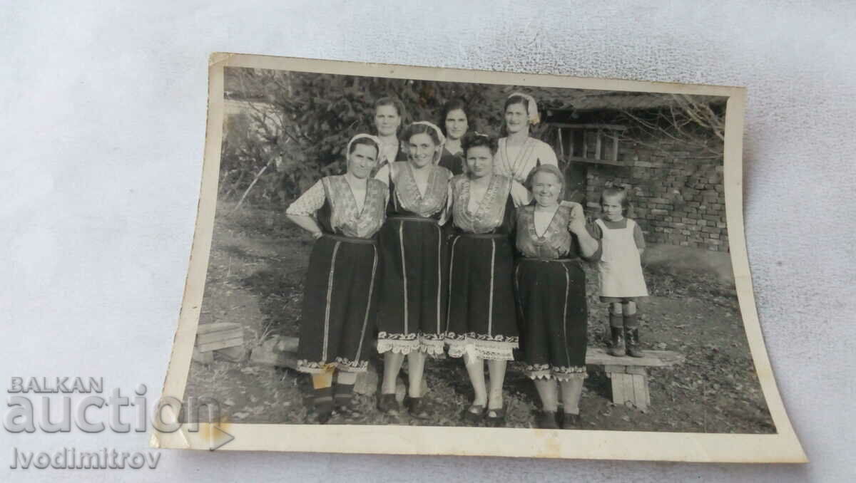 Foto Femei în costume tradiționale în curtea casei lui