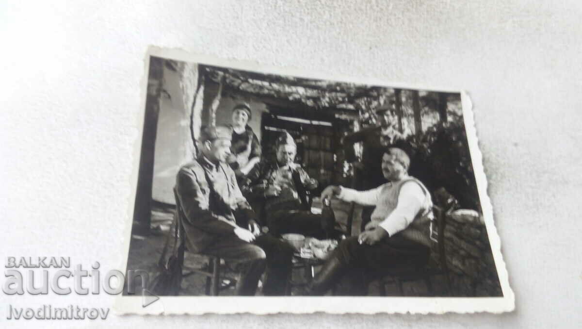 Fotografie cu un bărbat și doi soldați care beau ceva în curte