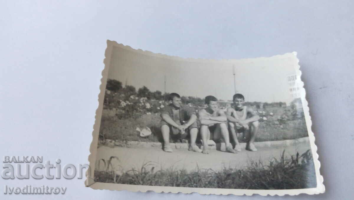 Φωτογραφία Τρεις νεαροί άνδρες που κάθονται στο πεζοδρόμιο