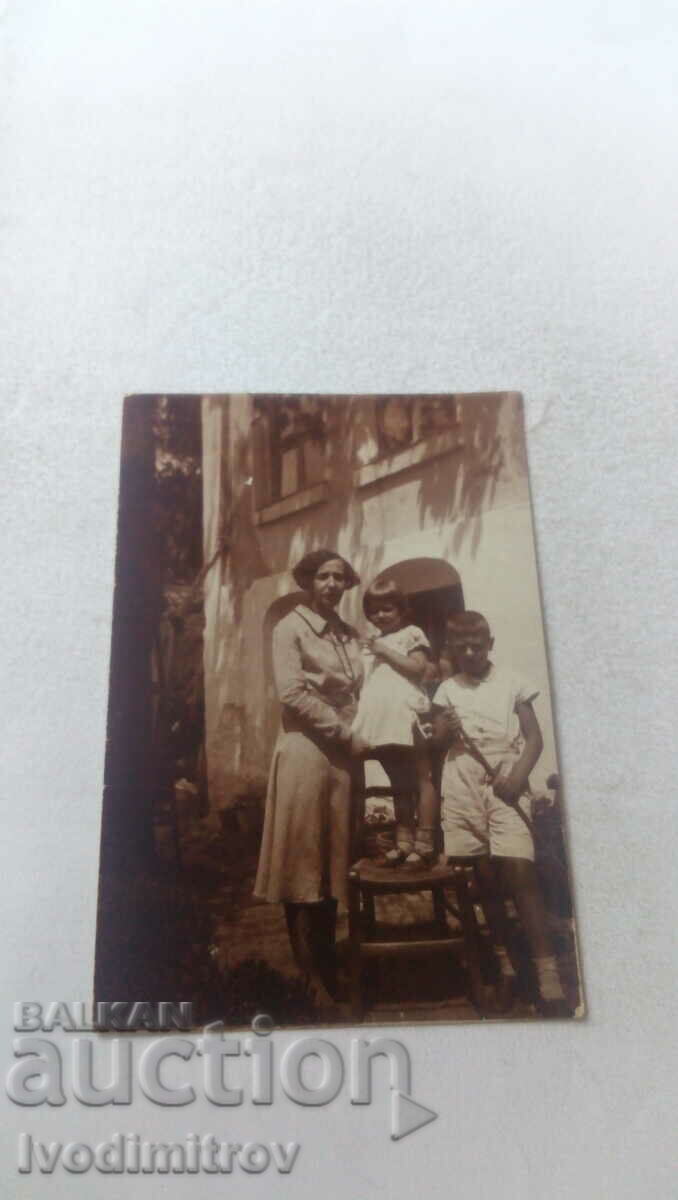 Photo A woman, a boy and a girl in the yard of their house