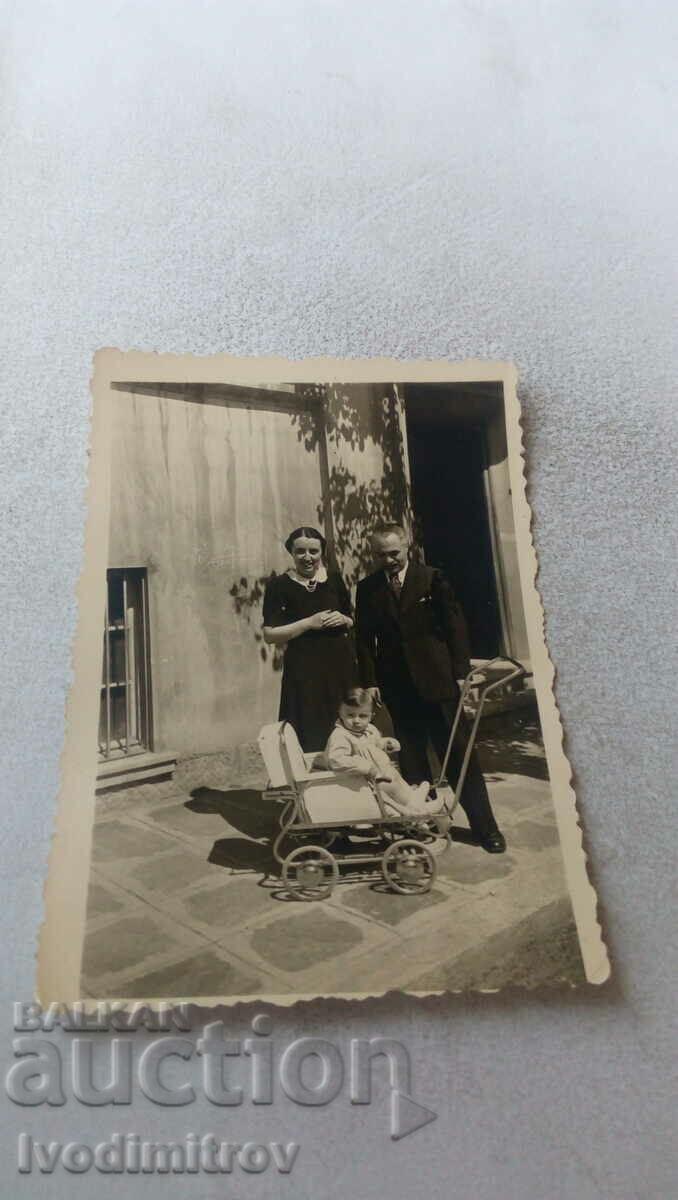 Fotografie Un bărbat, o femeie și un copil într-un cărucior de epocă în fața casei lor