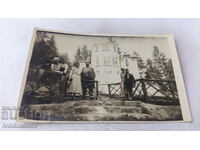 Photo A man, three women and two boys in front of a cottage in the mountains