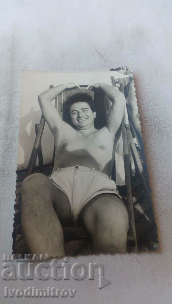 Photo A man in shorts lying on a wooden deck chair