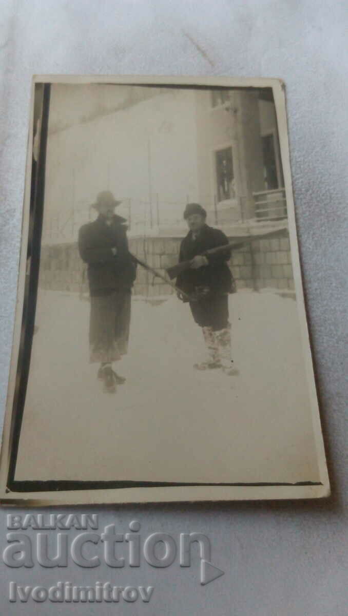 Foto Doi vânători în fața unei cabane iarna