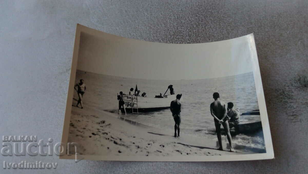 Fotografie Tineri pe malul mării lângă o barcă de lemn OTTER