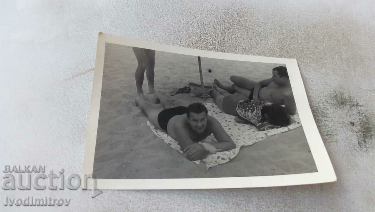 Foto Doi bărbați și o femeie pe un prosop pe plajă