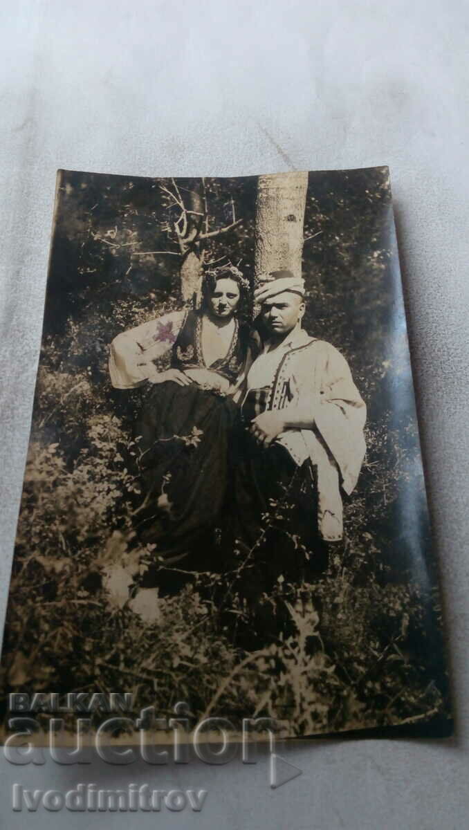 Photo A man and a woman in folk costumes by a tree in the forest