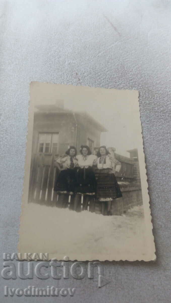 Снимка Три млади жени с народни носии до ограда през зимата