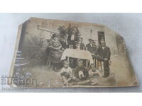 Picture Men, woman and children with three cats around a table