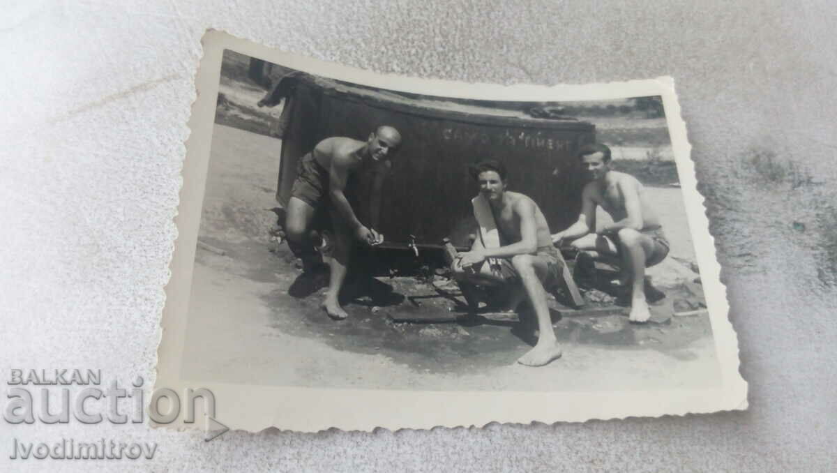 Photo Three men in shorts in front of a water tank