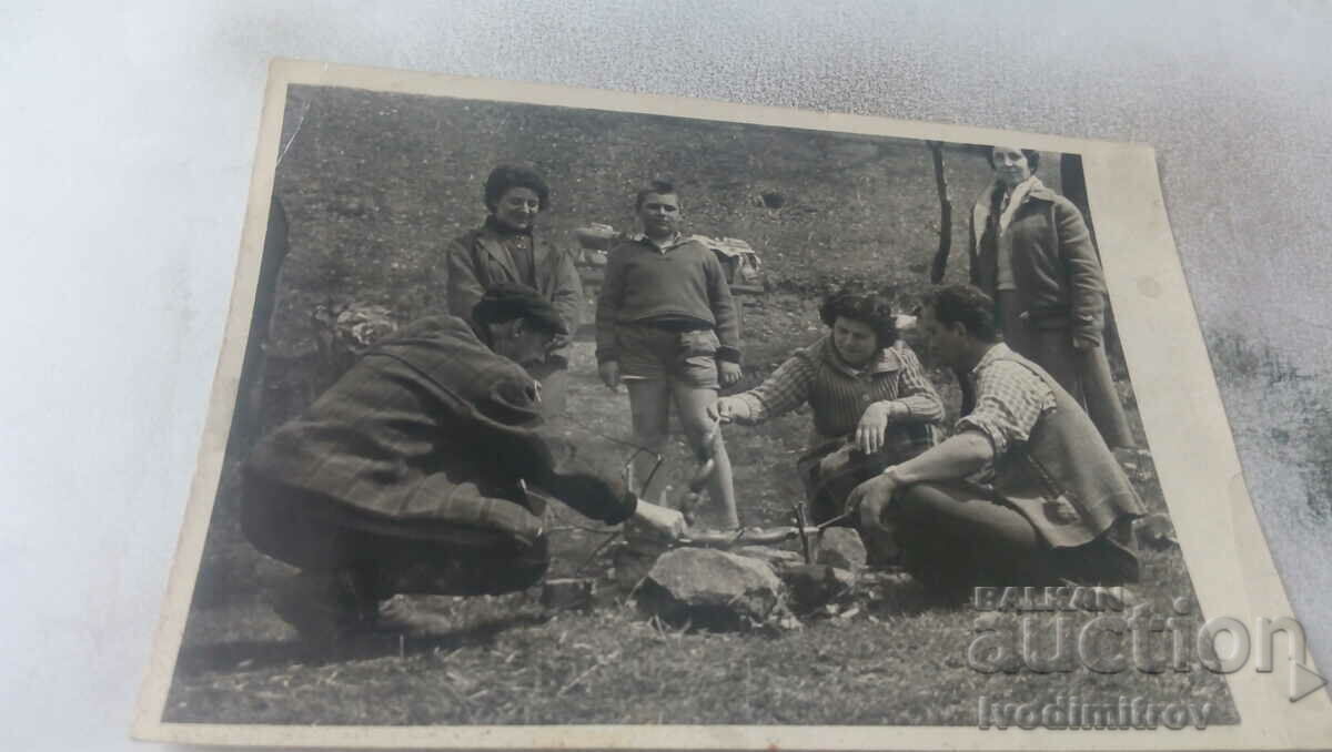 Photo Men, women and a boy roasting meat on a spit over a hearth, 1963