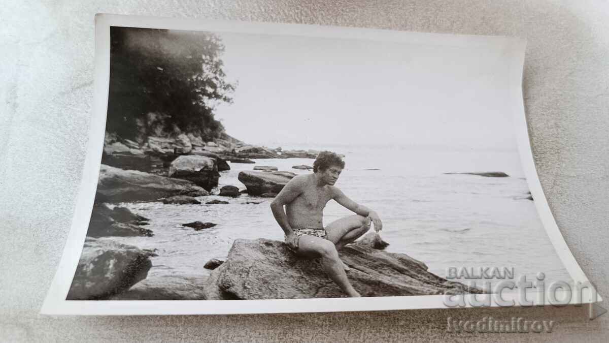 Photo A man in a swimsuit on a rock on the seashore