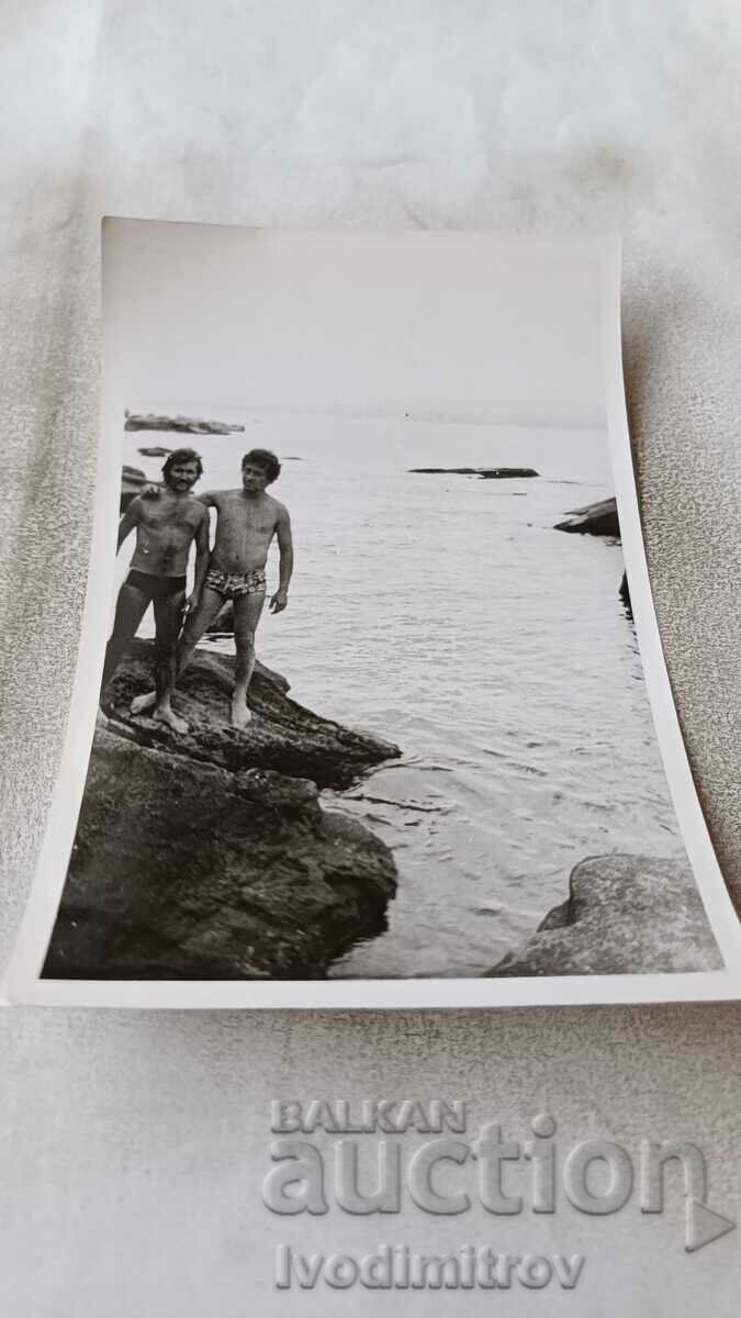 Φωτογραφία Δύο άντρες με μαγιό σε έναν βράχο στην παραλία