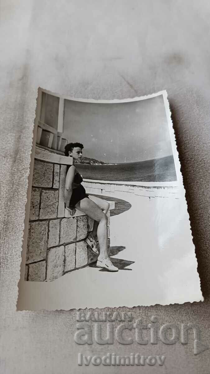 Foto Fată tânără în costum de baie așezată pe un zid de piatră