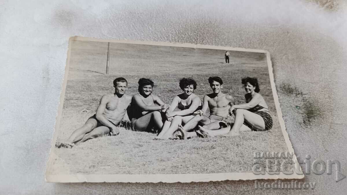 Снимка Младежи и млади жени по бански седнали на поляната