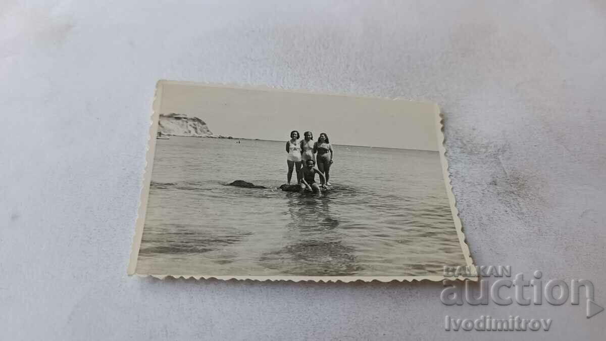 Φωτογραφία Ένας άνδρας και τρεις γυναίκες σε μια πέτρα στην παραλία