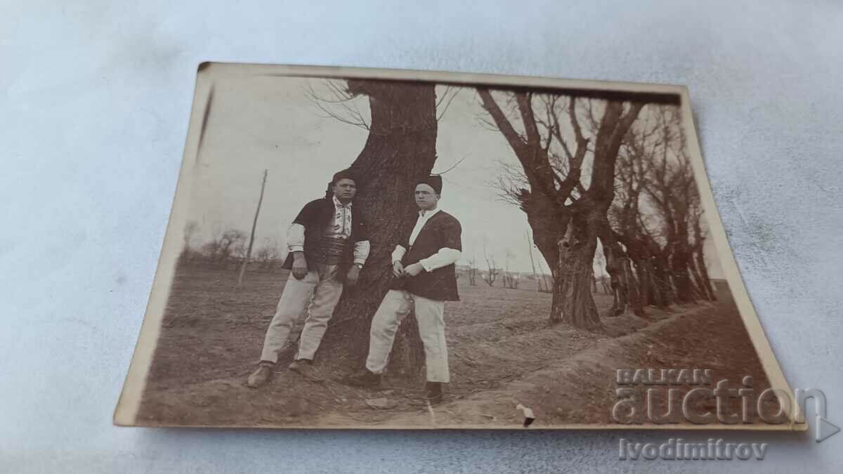 Photo Two men in folk costumes next to a tree