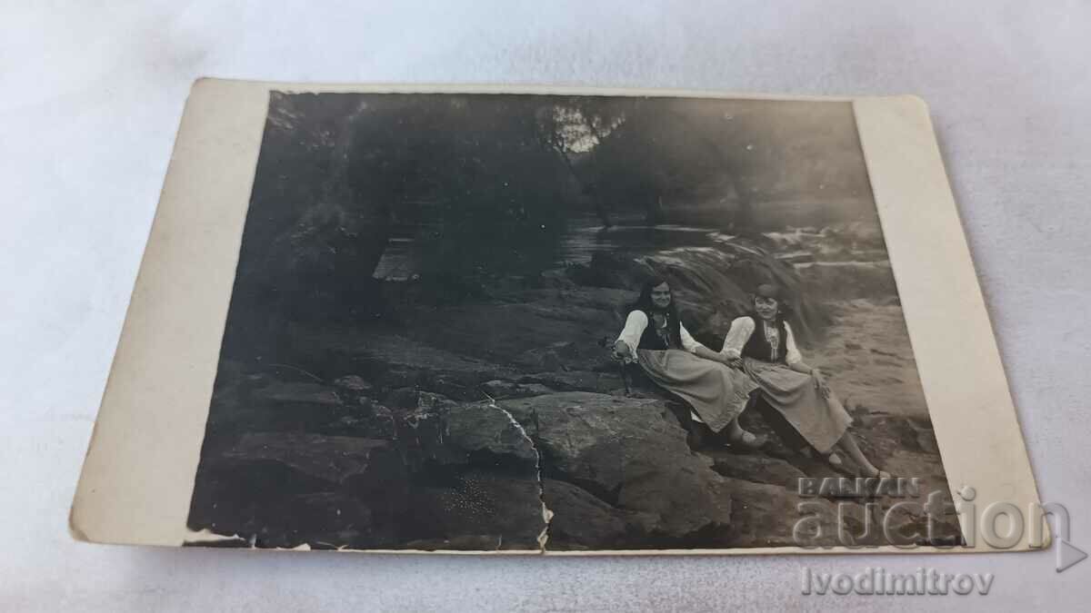 Photo Two young women in traditional costumes sitting by a stream