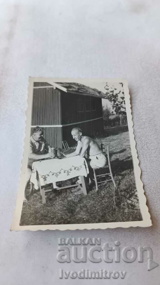 Photo Two men drinking beer in front of a bungalow