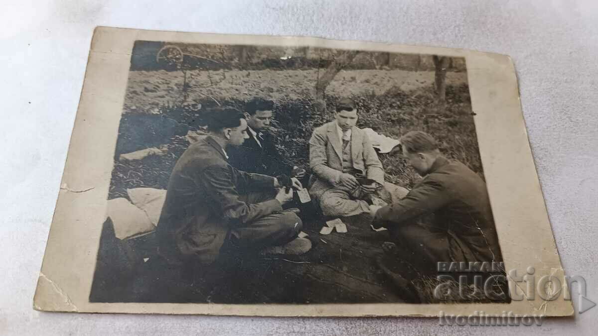 Φωτογραφία Τέσσερις νεαροί άνδρες που παίζουν χαρτιά σε ένα λιβάδι