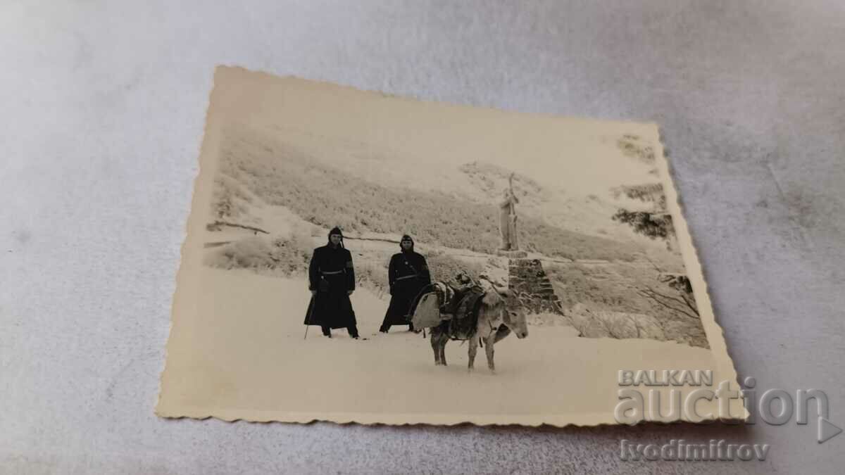 Photo Two soldiers with a donkey in front of a monument in the mountains