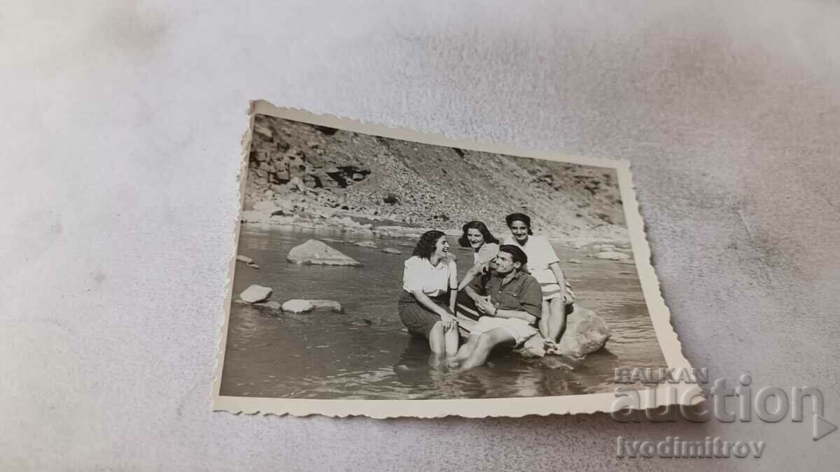 Φωτογραφία Ένας νεαρός άνδρας και τρία νεαρά κορίτσια σε μια πέτρα στο ποτάμι