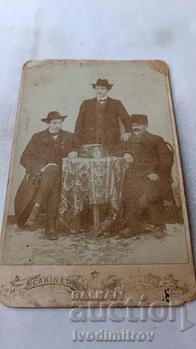 Photo Three men around a table with an alarm clock Cardboard
