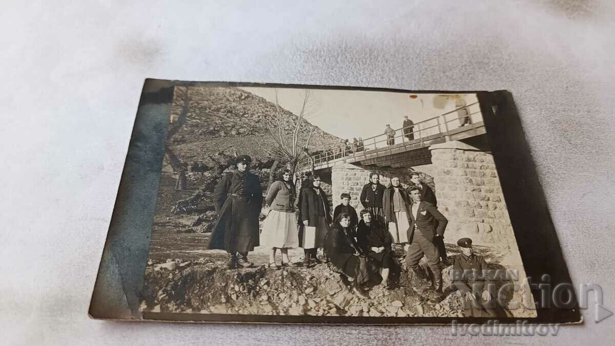 Photo Two soldiers, young men and women, by a bridge over a river