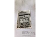 Prezentare generală a fotografiilor Trei copii mici mochi stând pe un foișor din lemn