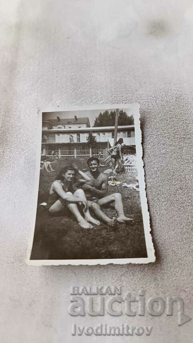 Photo A young man and a girl in swimsuits sitting on the grass