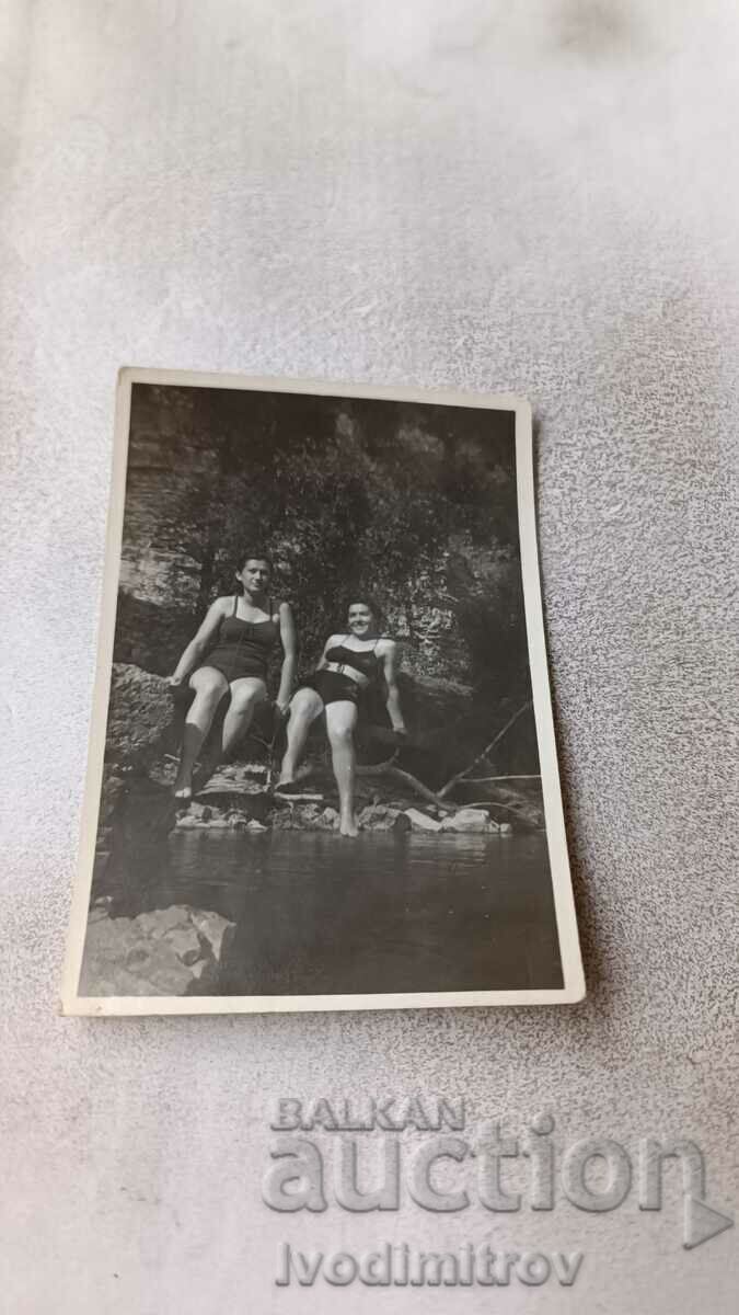 Mrs. Two young girls in swimsuits sitting on a rock by the sea