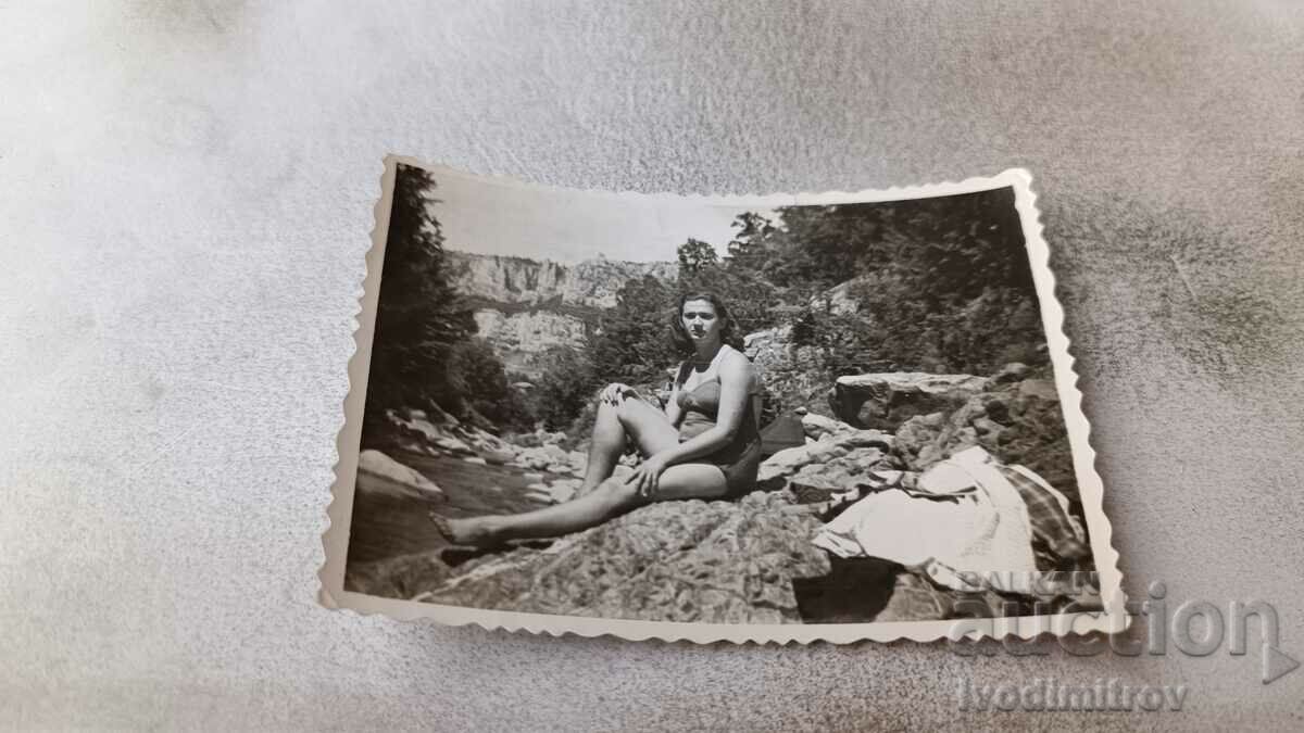 Fotografie O fată tânără în costum de baie așezată pe o stâncă lângă mare