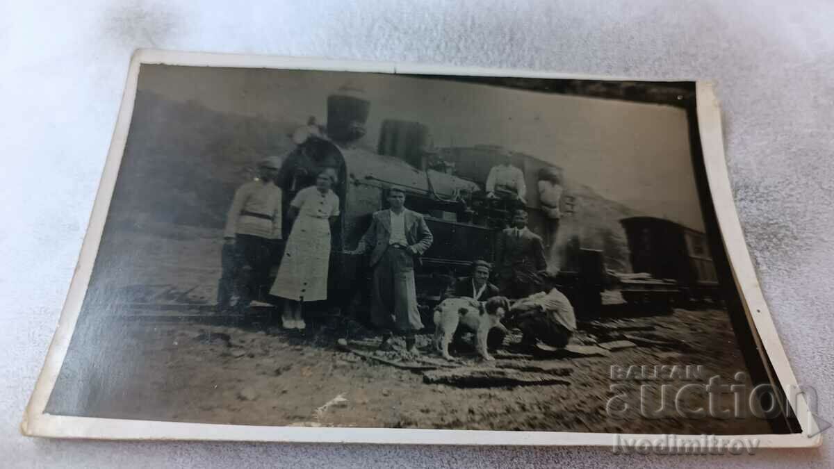 Photo Men, women and a dog in front of a steam locomotive