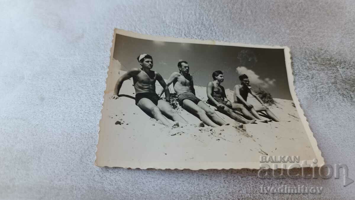 Foto Trei bărbați și o femeie în costume de baie stând pe dună