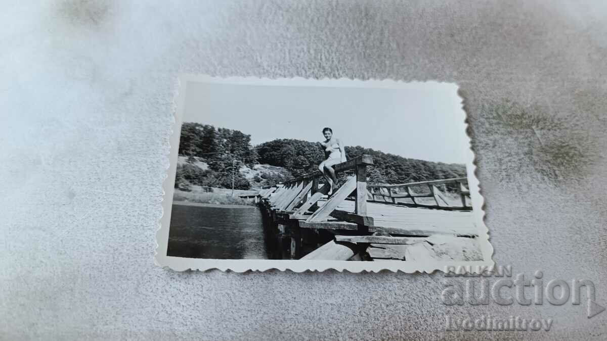Φωτογραφία Ένα νεαρό κορίτσι με μαγιό που κάθεται στο κιγκλίδωμα μιας γέφυρας