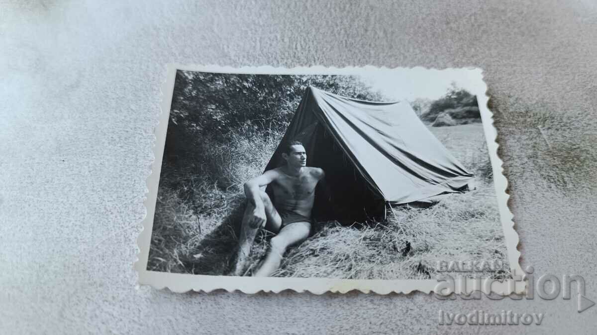 Photo A young man in a swimsuit sitting in front of a tent