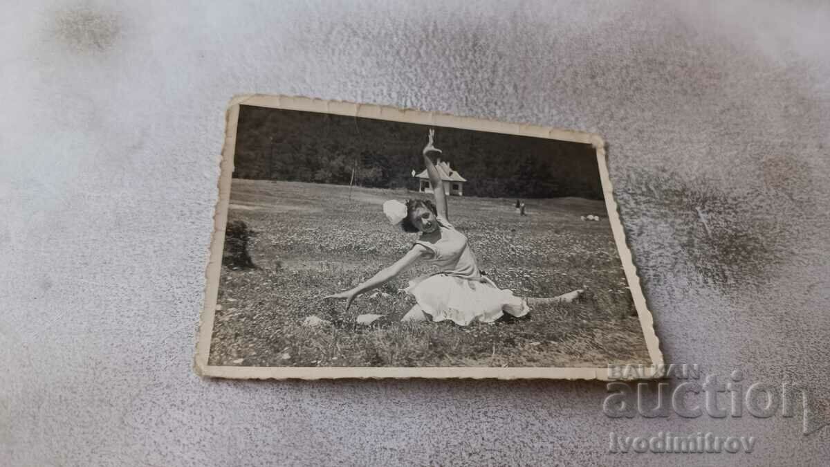 Fotografie O fată tânără într-o rochie albă face o ghemuială pe gazon