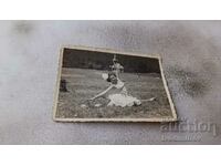 Снимка Младо момиче с бяла рокля правеща щпагат на поляната