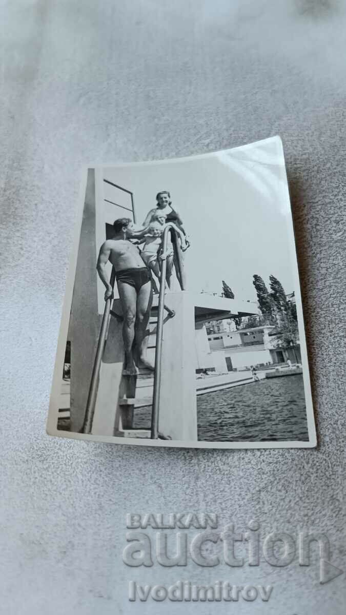 Photo Men, woman and two children on a diving board in a swimming pool