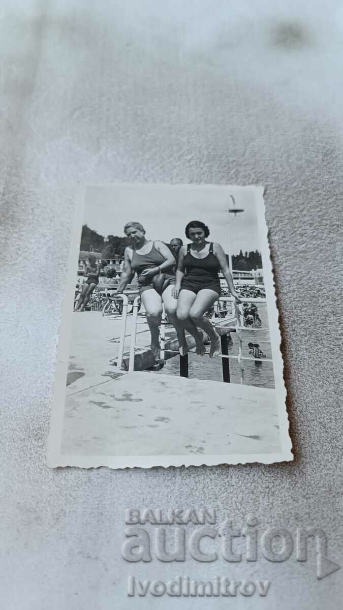 Photo Two women in swimsuits sitting on the railing of a swimming pool