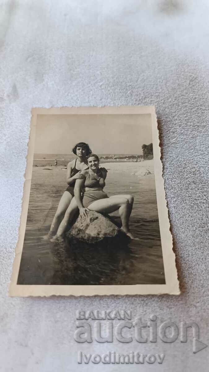 Photo Two young girls sitting on a rock in the sea