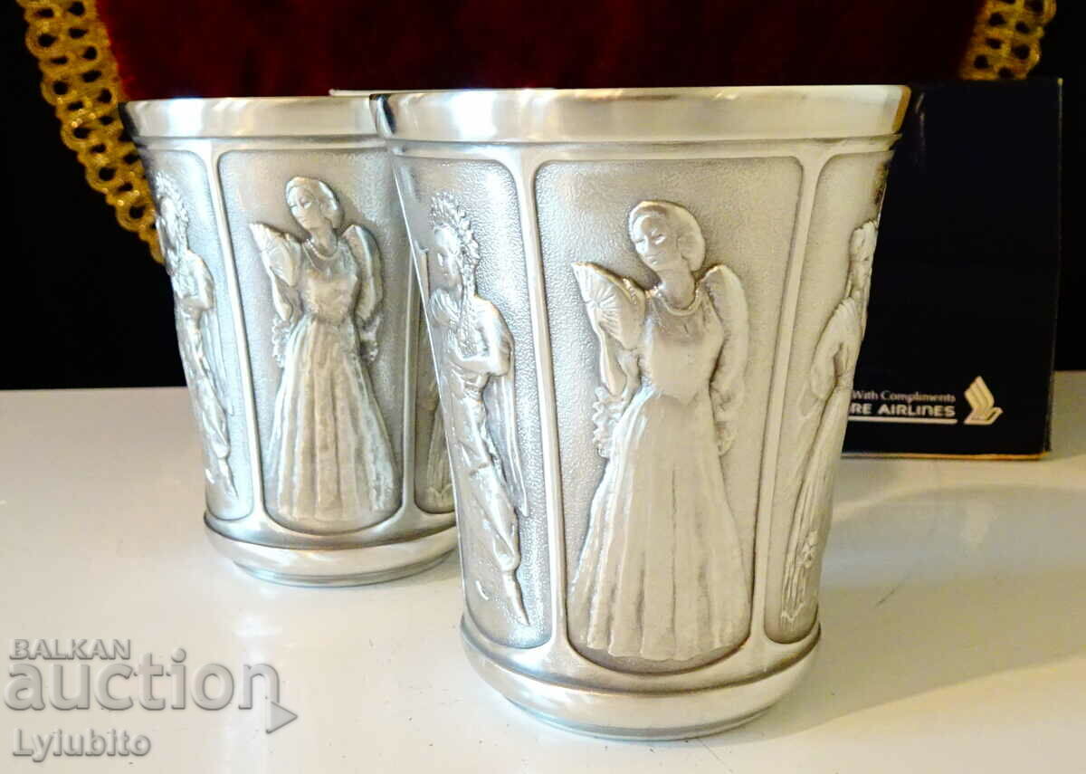 Two pewter cups with female dancers from different cultures.